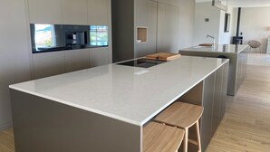 A modern kitchen with a central island, wooden stools, and a built-in oven. - VILLA PORTICCIO SWIMMING POOL EXCEPTIONAL SEA VIEW - BEACH 5 mn -GARDEN LANDSCAPE (Corse)