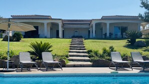 A pool area with lounge chairs, a clear sky, and a building with columns and a tiled roof. - VILLA PORTICCIO SWIMMING POOL EXCEPTIONAL SEA VIEW - BEACH 5 mn -GARDEN LANDSCAPE (Corse)
