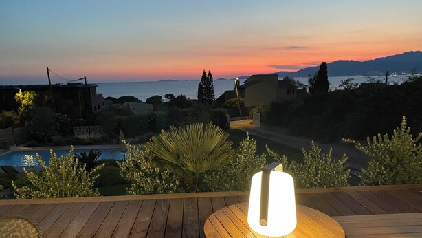 A wooden deck with a round table and chairs, overlooking a swimming pool and a sunset view. - VILLA PORTICCIO SWIMMING POOL EXCEPTIONAL SEA VIEW - BEACH 5 mn -GARDEN LANDSCAPE (Corse)