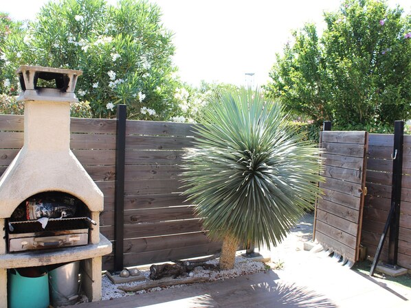 A patio area with a stone barbecue grill, a wooden fence, and a yucca plant.