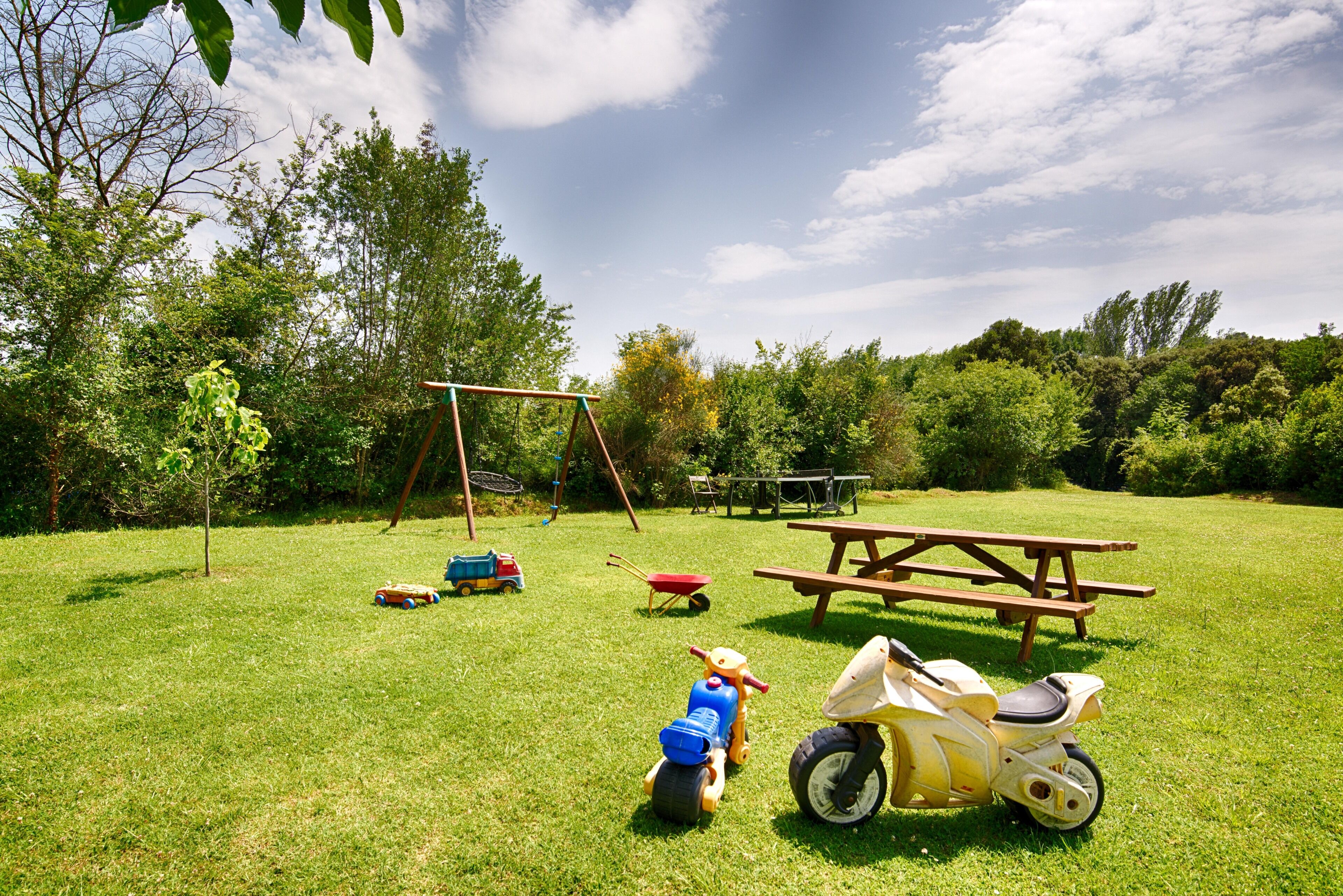 A grassy outdoor area with a picnic table, a swing set, and children's toys.