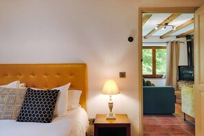 A bedroom with a bed, a nightstand with a lamp, a sofa, and a stone fireplace.