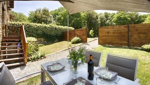 Un espacio de comedor al aire libre con una mesa preparada para dos, una botella de vino y un jarrón con flores.