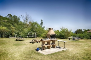 An outdoor barbecue area with a stone chimney, picnic tables, and a swing set. - Mountain View | Stylish Apt | Luxury Bath | Forest (Sales De Llierca)