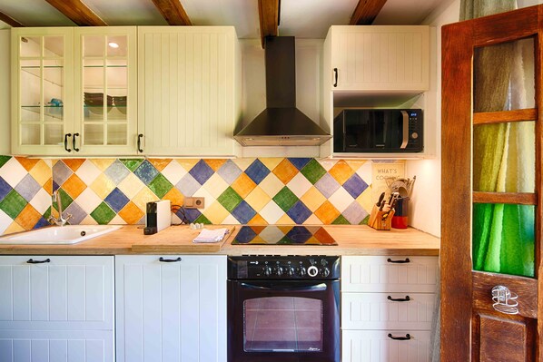 A kitchen with white cabinets, a microwave, a stove, and a colorful tile backsplash. - Mountain View | Stylish Apt | Luxury Bath | Forest (Sales De Llierca)