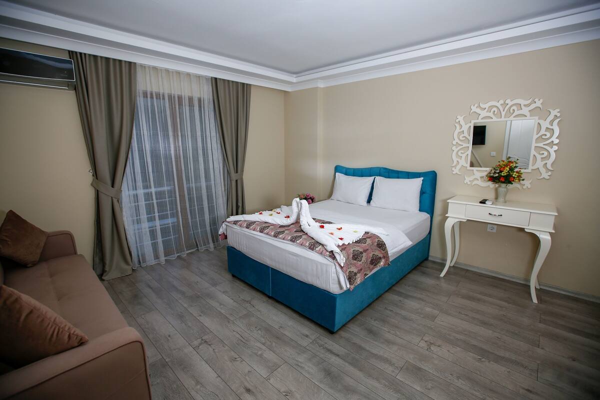 A hotel room with a large bed, a bedside table, a mirror, and a sofa.