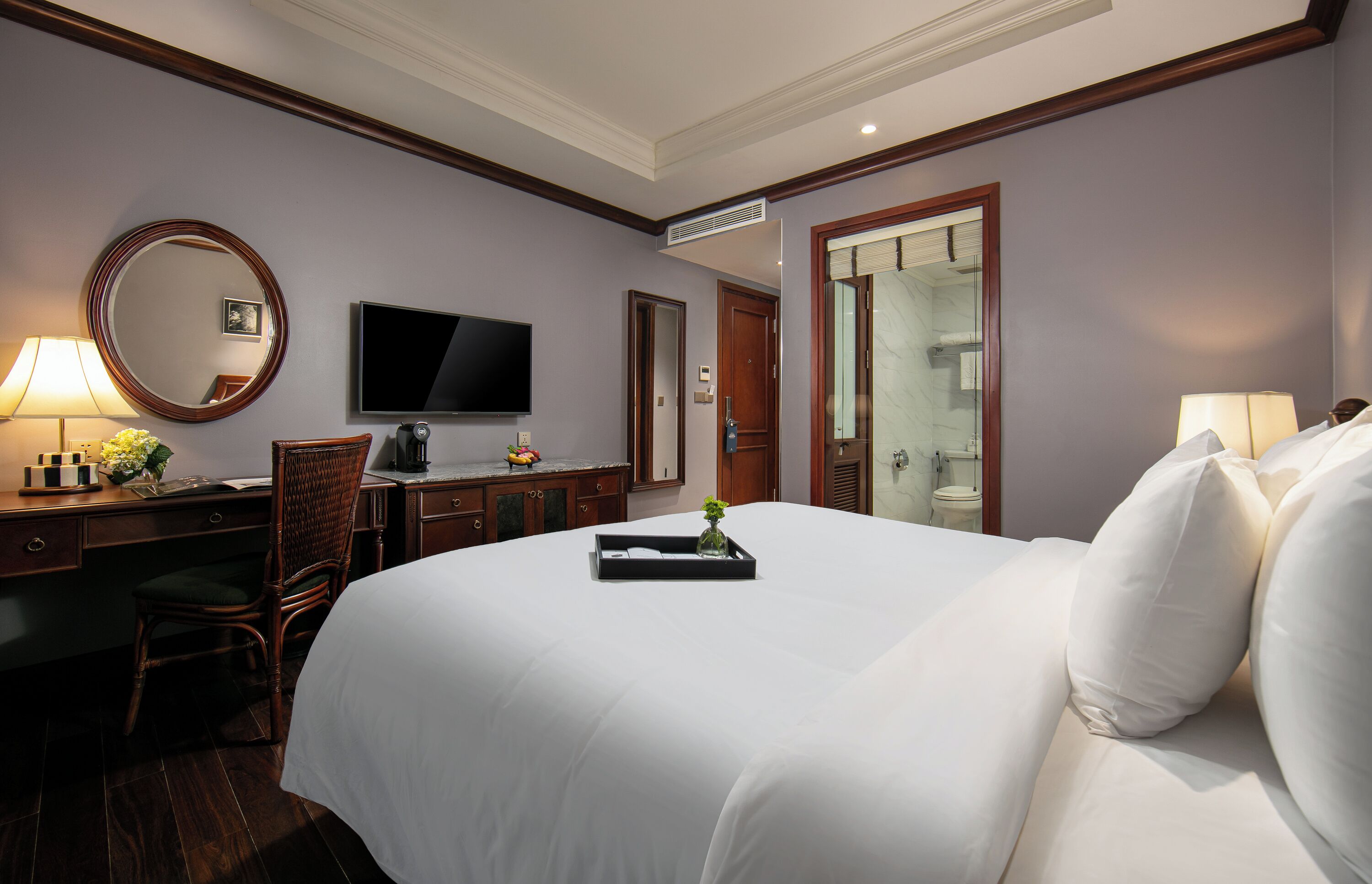 Ein Hotelzimmer mit einem großen Bett, einem Schreibtisch mit Stuhl, einem Fernseher und einem durch eine offene Tür einsehbarer Badezimmer.