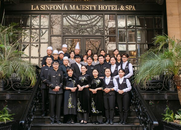 Un grupo de personas frente al hotel y spa La Sinfonía Majesty, con una fachada decorativa y escalones que conducen a la entrada.