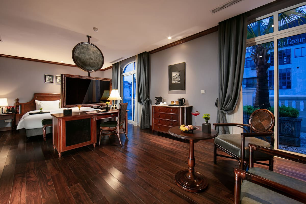 Habitación de hotel con cama, escritorio, silla y un ventanal con vista a edificios.