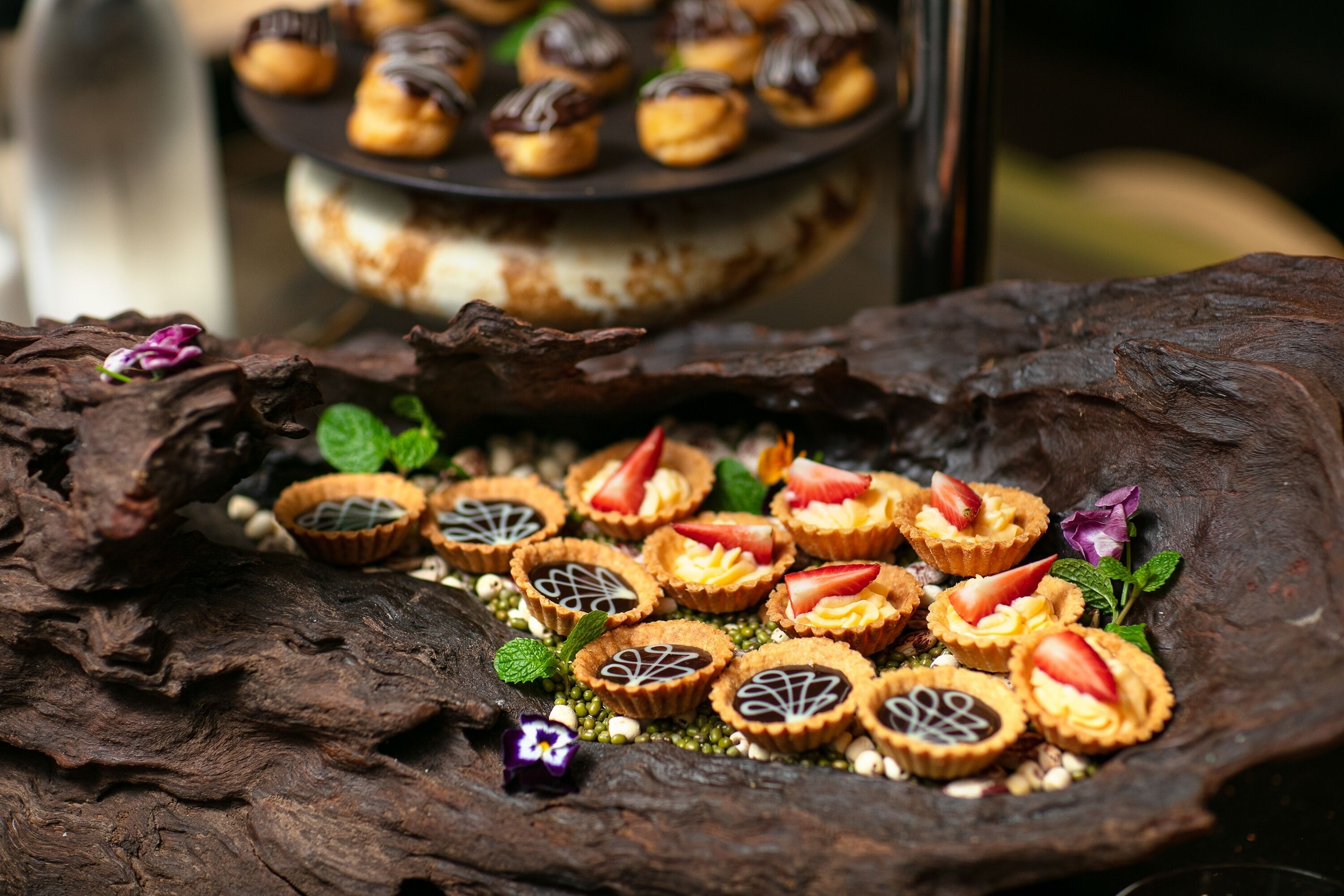 A variety of desserts on a rustic wooden surface, including tarts with strawberries and mint leaves.