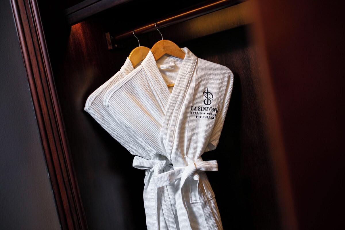Una bata blanca con la inscripción 'LA SINFONI HOTELS & RESORTS VIETNAM', colgada de una percha de madera.