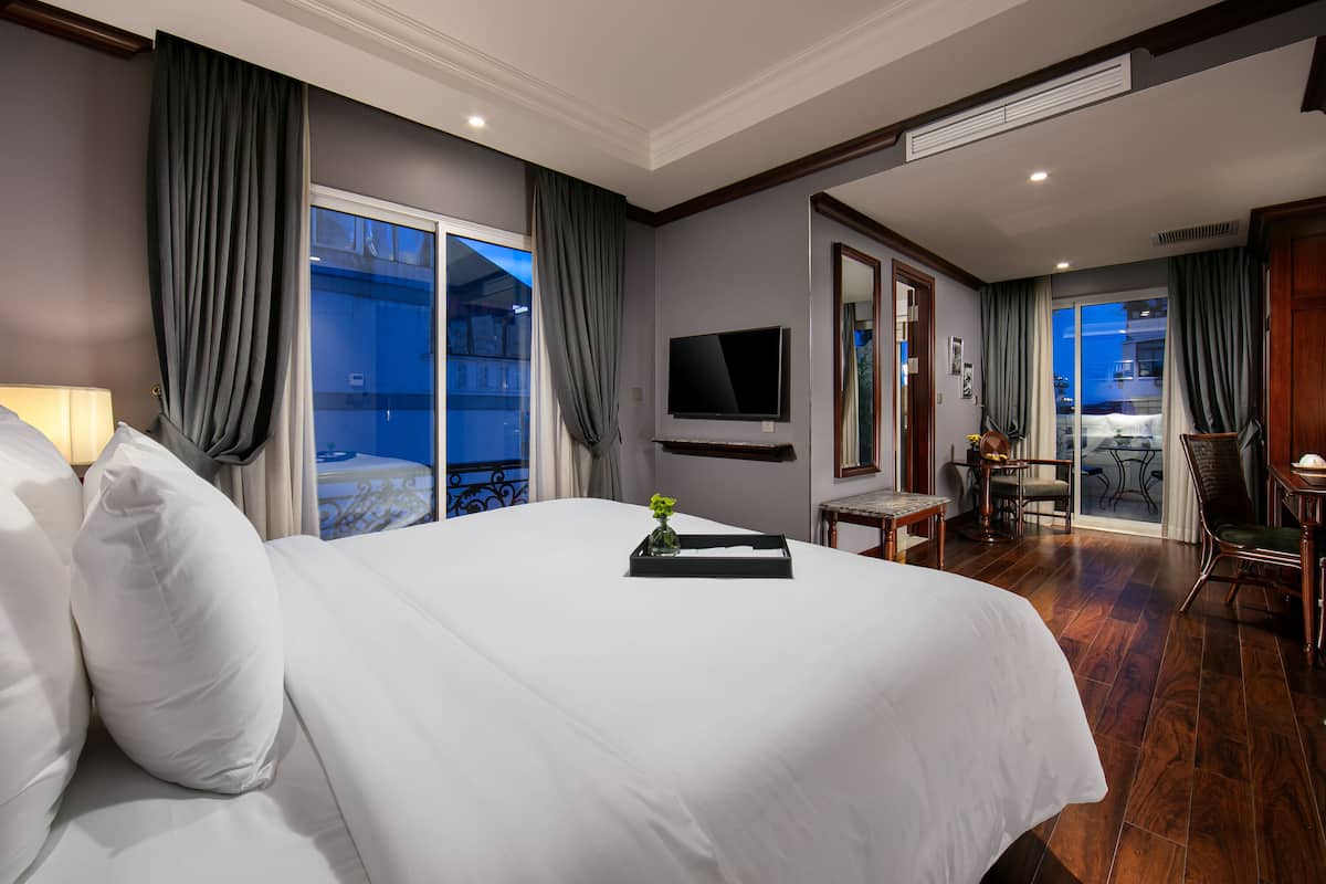 Habitación de hotel con una cama grande, un televisor montado en la pared y un balcón con vistas a la ciudad.