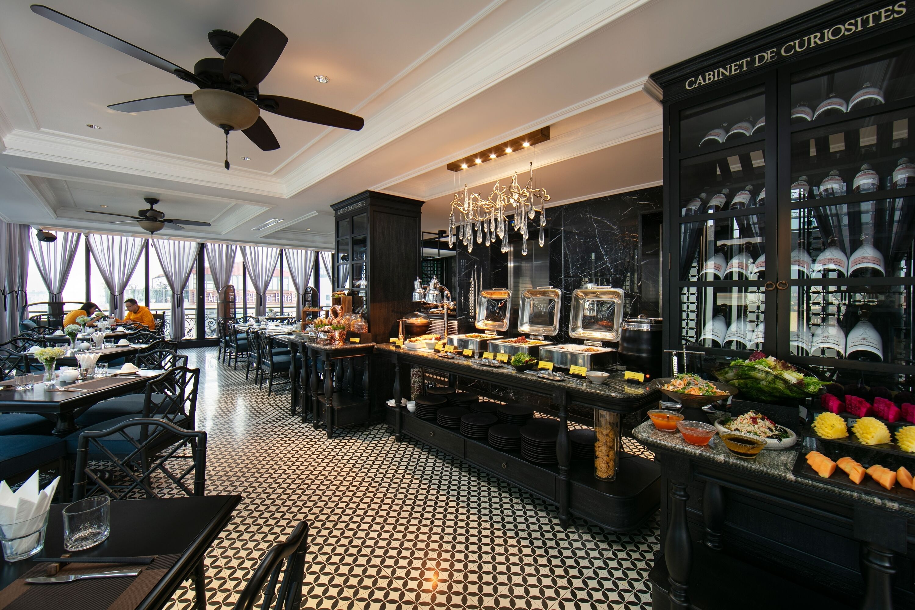 A restaurant with a black and white tiled floor, a buffet counter with various food items, and a ceiling fan.
