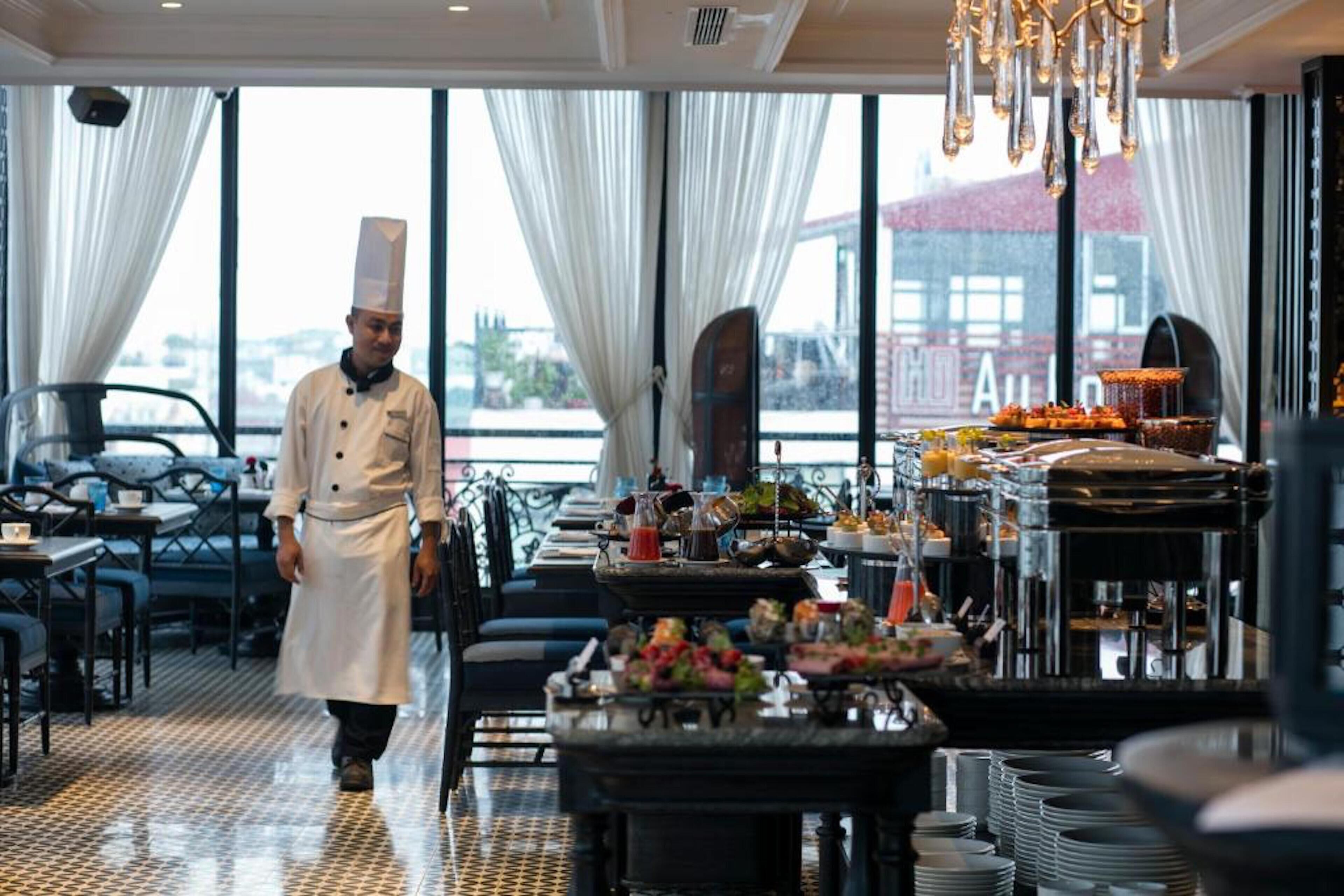 A restaurant with a chef walking through, large windows, and a buffet setup.