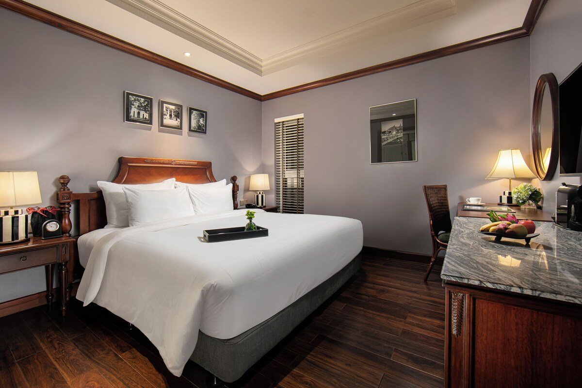 Habitación de hotel con una cama grande, mesitas de noche, un escritorio con silla, un espejo y cuadros en la pared.