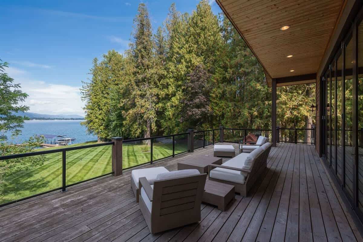 Eine Holzterrasse mit Gartenmöbeln, mit Blick auf einen See und einen Wald.