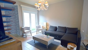 A modern living room with a grey sofa, white armchairs, a coffee table, and a chandelier. - West Flanders Vacation Home (Comines-Warneton)