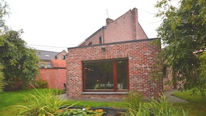 A brick house with a large window, surrounded by a garden with a pond and tall grasses. - West Flanders Vacation Home (Comines-Warneton)