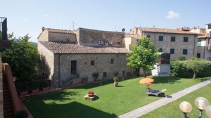 A courtyard with stone buildings, a lawn, and a small seating area with a table and chairs. - Cottage in Chianti With Pool & Vineyard Views (Barberino Tavarnelle)