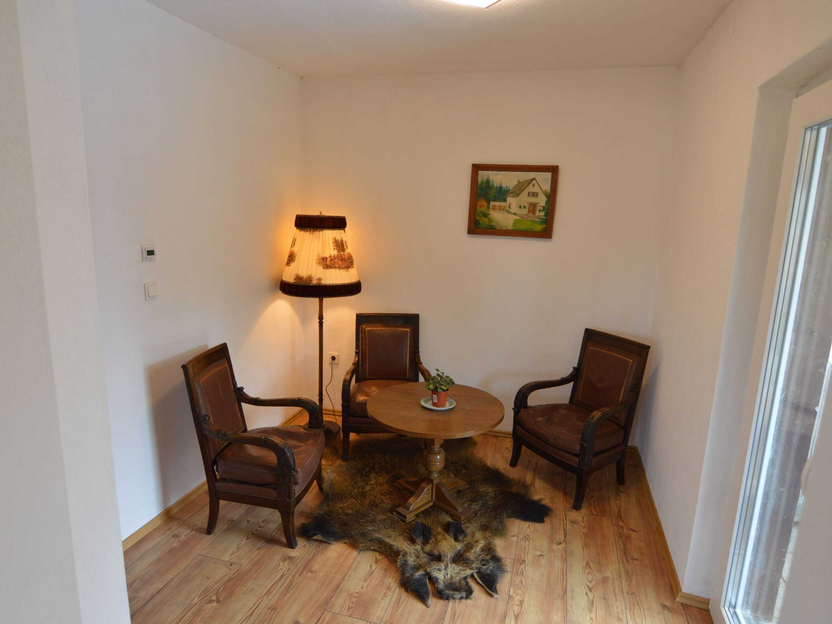 A room with a round wooden table, two chairs, a floor lamp, and a painting on the wall.