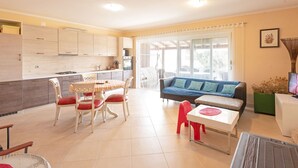 A modern kitchen with white cabinets, a dining table with red chairs, and a blue sofa in a bright living area with large windows. - Modern Holiday Home in Mandre With Barbeque (Zmijavci)