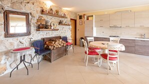 A cozy living area with a stone wall, a fireplace, a dining table with chairs, and a kitchen with wooden cabinets. - Modern Holiday Home in Mandre With Barbeque (Zmijavci)