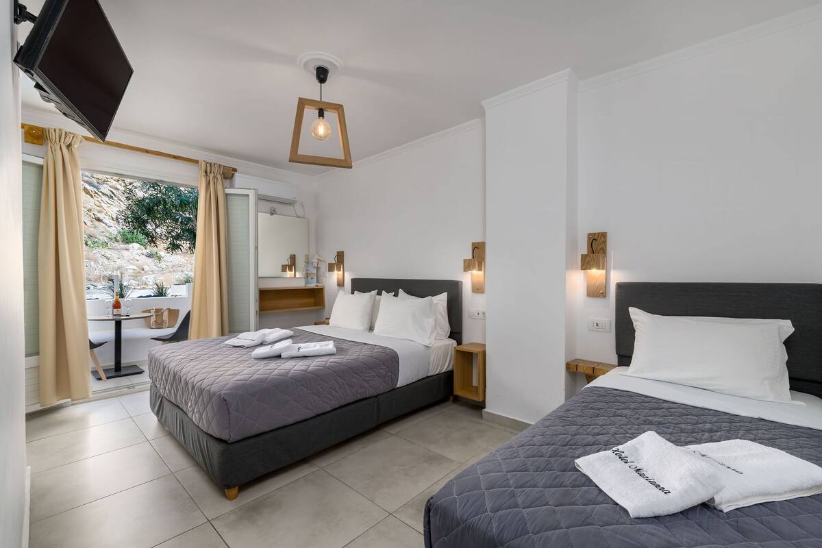 A hotel room with two beds, a TV, a desk with a chair, and a view of the outdoors.
