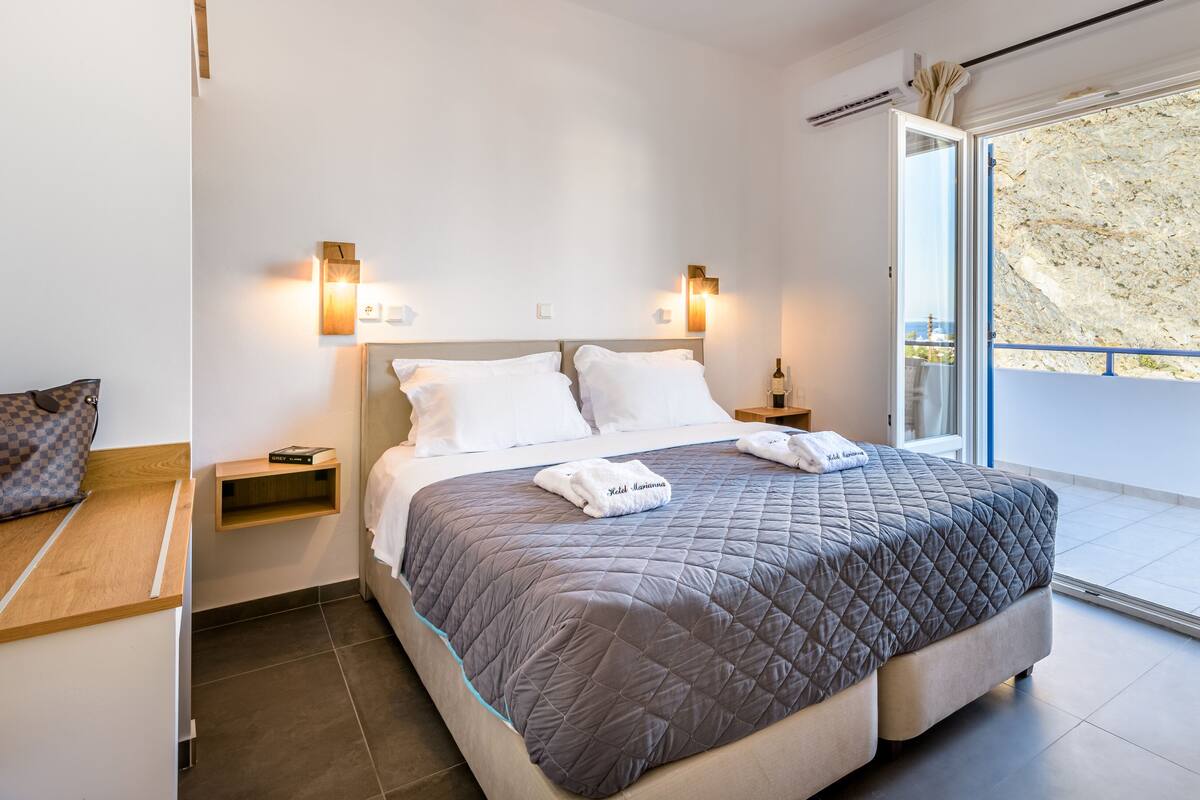 A modern hotel room with a large bed, two bedside tables, a nightstand, and a balcony with a view of the beach.