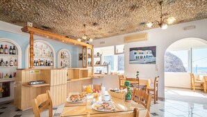 Een ontbijtsetting met een houten tafel, stoelen en diverse ontbijtartikelen. Er is een bar met flessen en een bord dat een waarschuwing aanduidt.