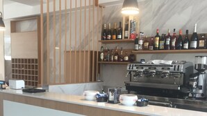 Zona de bar con mostrador de madera, una máquina de café y estantes con diferentes botellas.