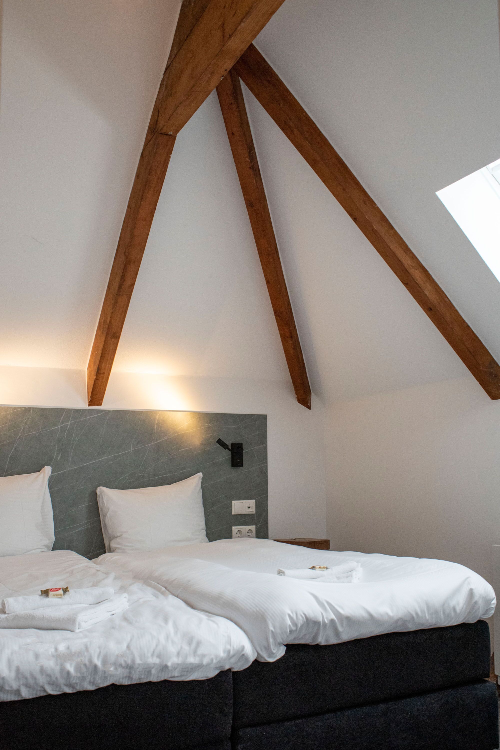Een slaapkamer met een schuine plafond, een bed met witte beddengoed, een stenen hoofdbord en een dakraam.