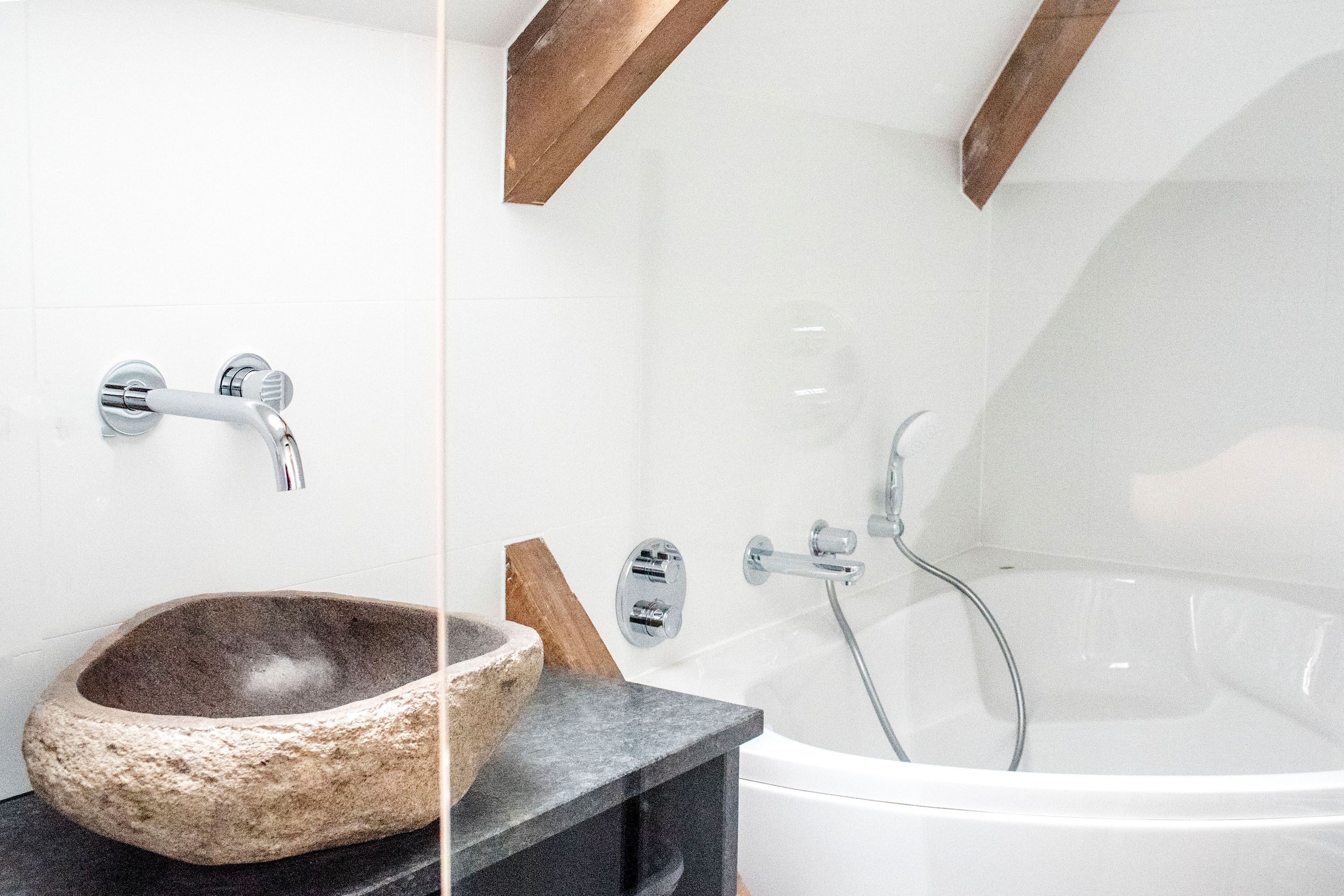 A modern bathroom with a stone basin, a black countertop, and a white bathtub with chrome fixtures.