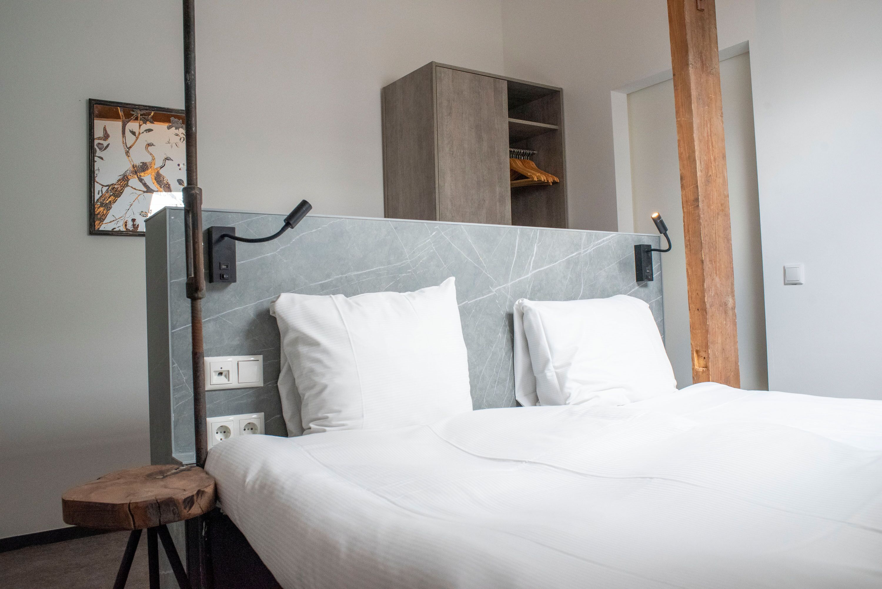 Une chambre à coucher moderne avec un grand lit, un tabouret en bois, une armoire et un luminaire fixé au mur.
