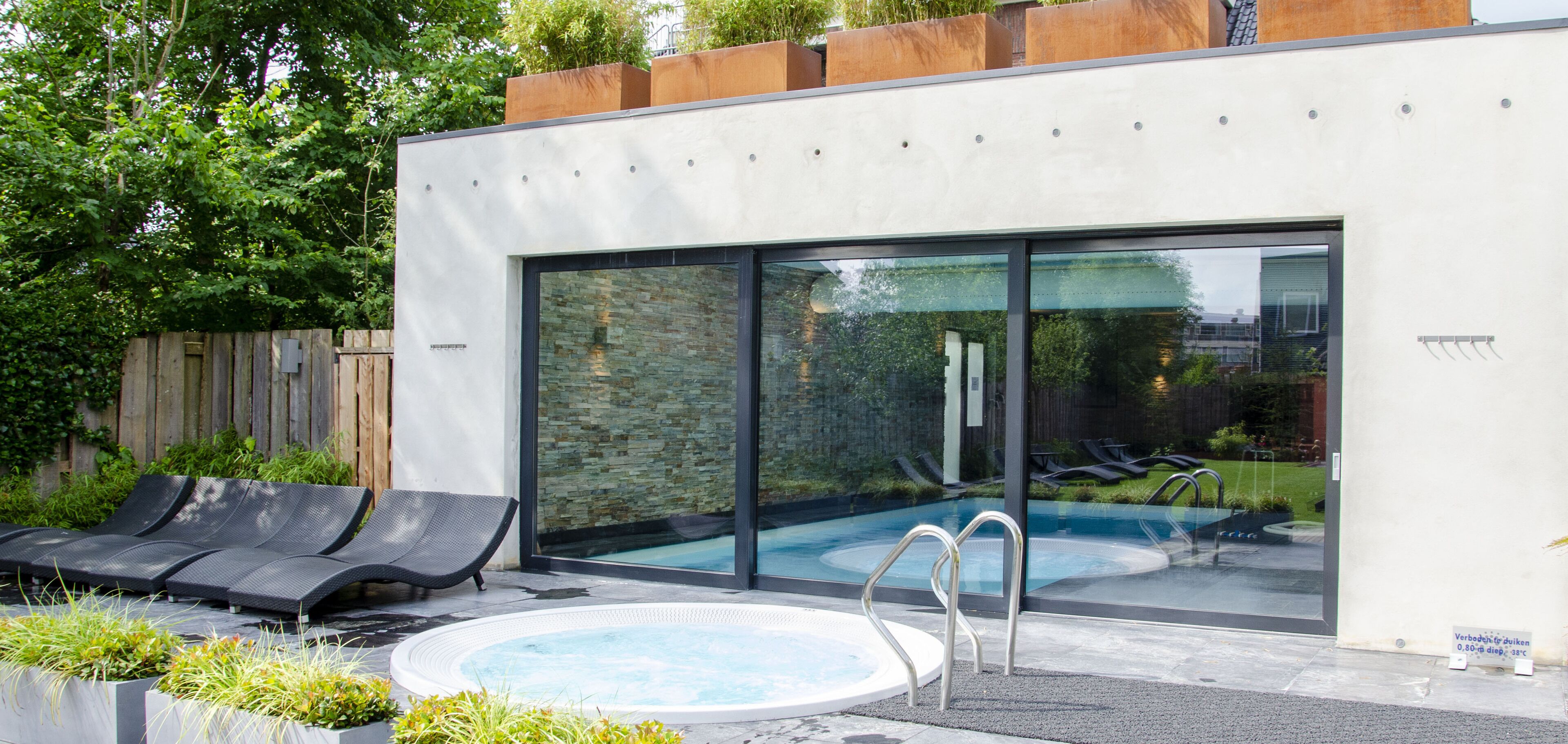 A modern outdoor pool area with lounge chairs, a hot tub, and a glass-enclosed pool.