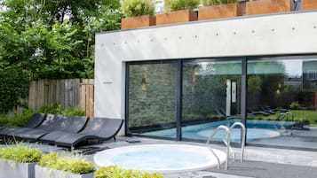A modern outdoor pool area with lounge chairs, a hot tub, and a glass-enclosed pool.
