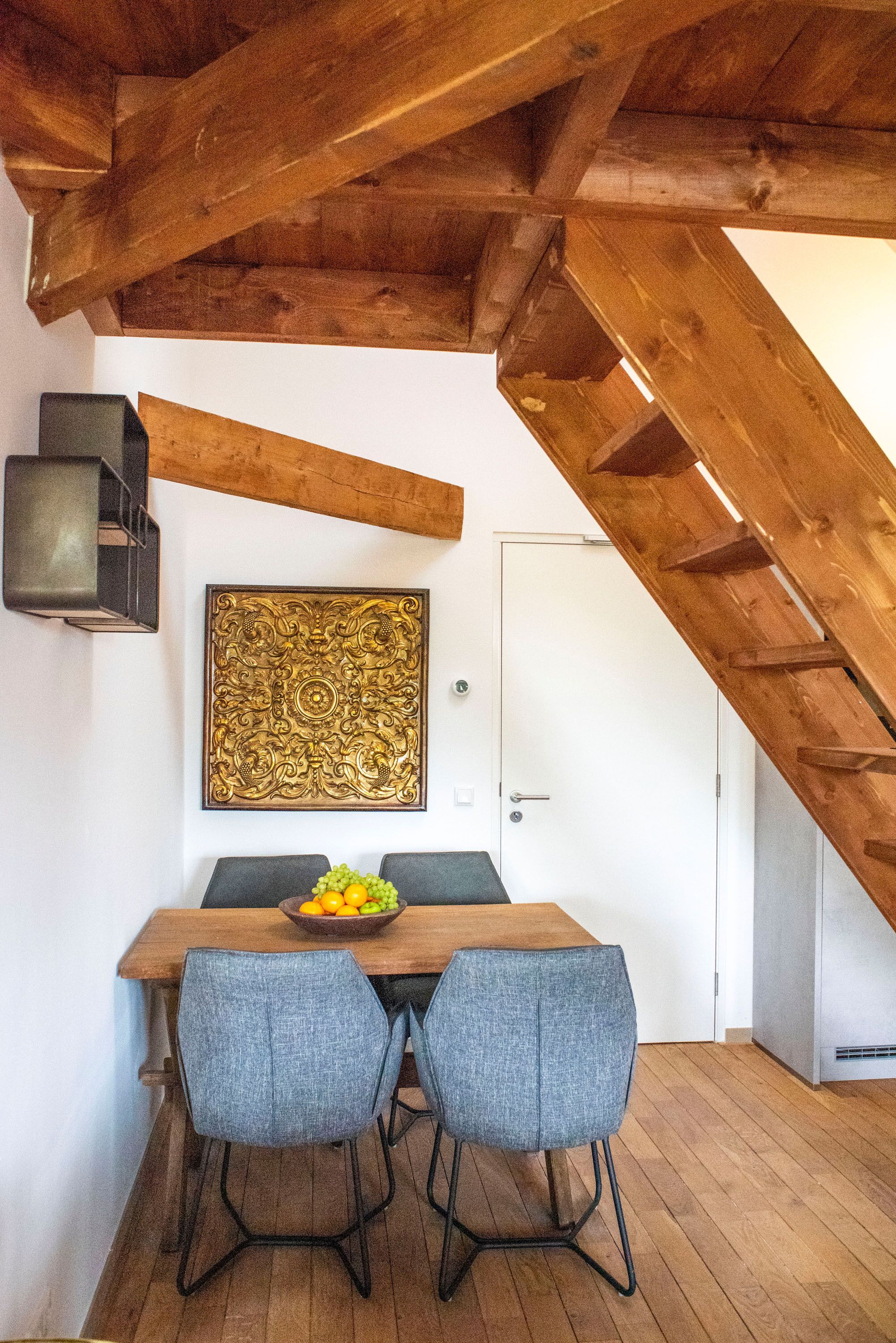 Uma sala de jantar com uma mesa de madeira, duas cadeiras, um objeto decorativo na parede e uma porta branca.