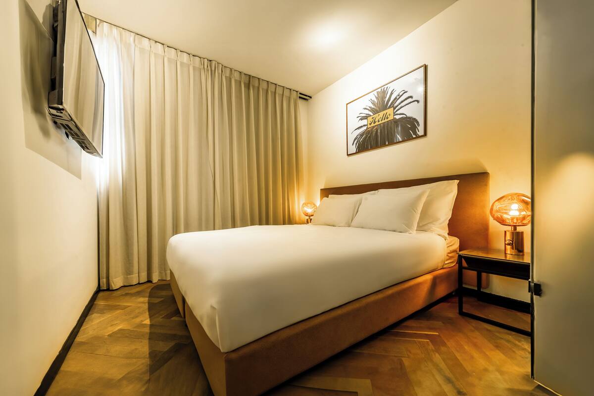 Een hotelkamer met een bed, een aan de muur bevestigde televisie, een bedlampje en een ingelijst schilderij.
