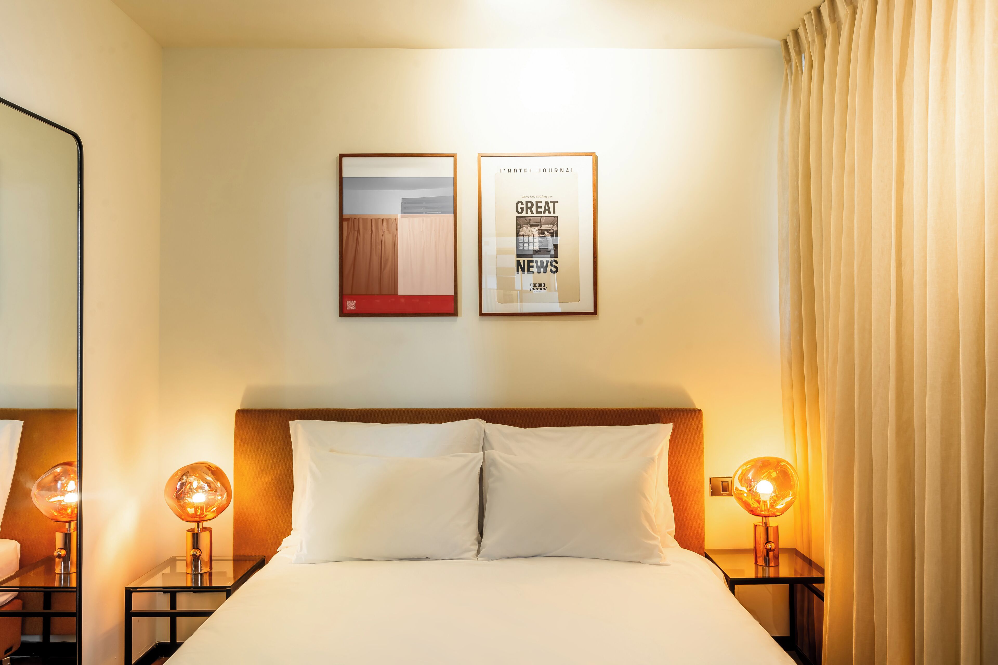 Habitación de hotel con cama, dos mesitas de noche, dos lámparas de pared, un espejo y dos cuadros enmarcados.