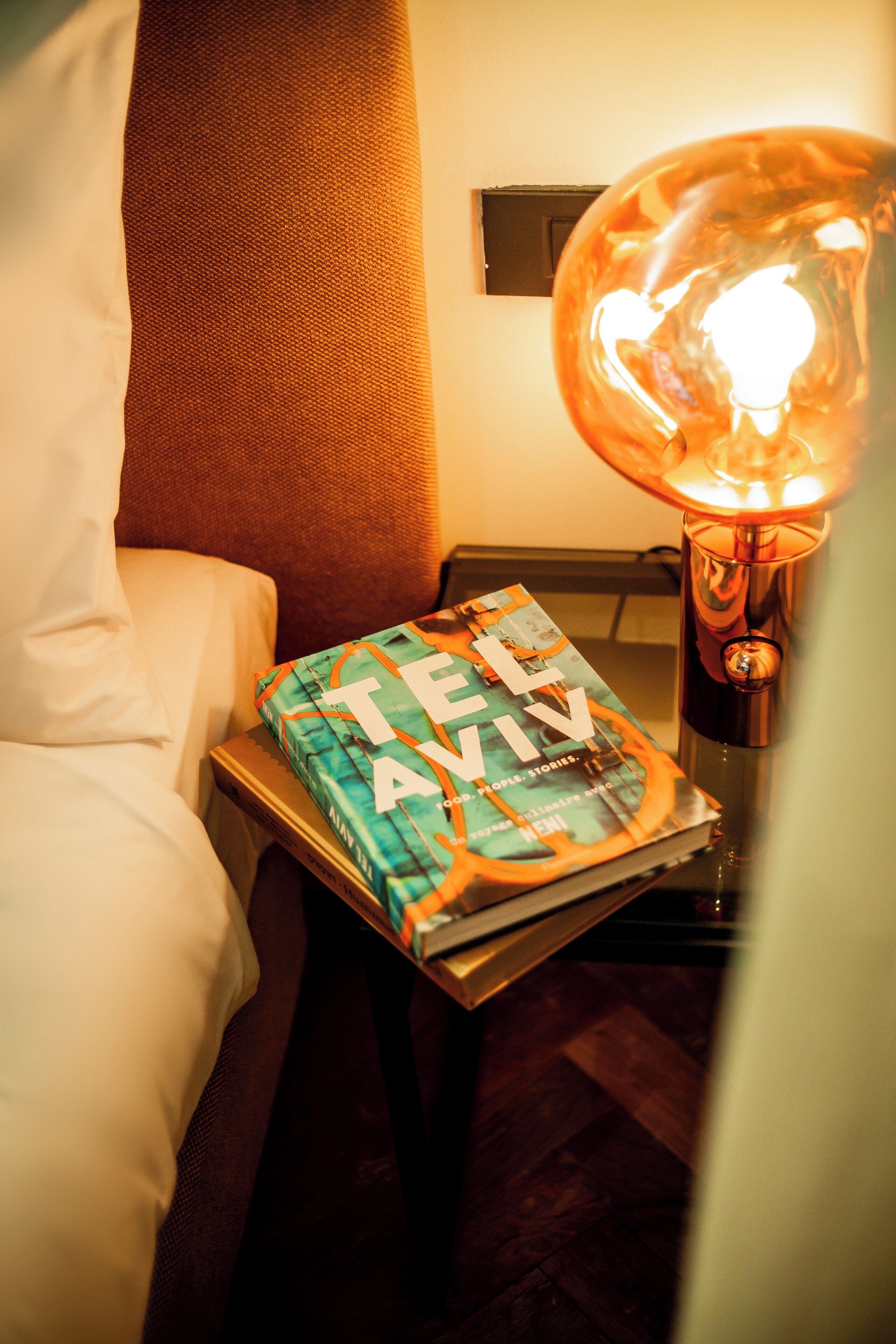 A bed with a pillow, a bedside table with a lamp, and a book titled 'TELLY' on the table.