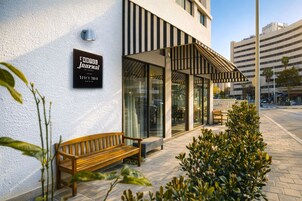 Un edificio moderno con una banca en el exterior, un letrero que dice 'L'MODE Journal' y un área de estar al aire libre cubierta.