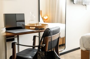 Una habitación de hotel con escritorio, ordenador portátil, silla, mesita de noche, lámpara y cama.