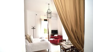 A hotel room with a bed, a red sofa, a dining table with chairs, a television, and a hanging light fixture. - VILLA LA PINETA DI SINALUNGA - Valdichiana and Val d'Orcia for family or friends (SINALUNGA)