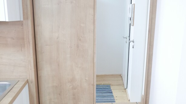 A wooden wardrobe with a mirror, a hat hanging on the door, and a shoe rack below. - Stadthaus Franz Josef (Hallein)