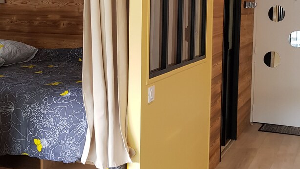 A modern bedroom with a wooden headboard, a bed with a floral bedspread, a yellow accent wall, and a large window. - Elegant and modern, at the foot of Mt-Blanc (Saint-Gervais-les-Bains)