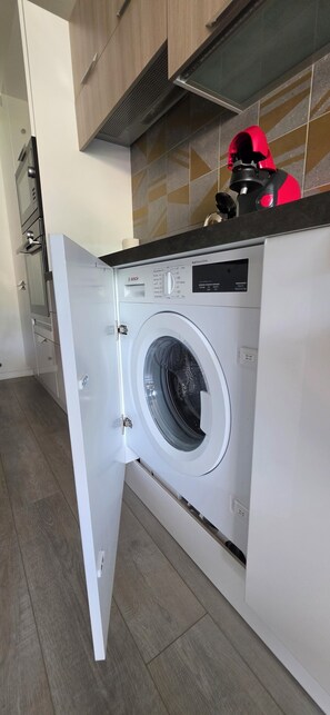 Een moderne keuken met een Bosch wasmachine, houten kastjes en een betegelde spatwand.