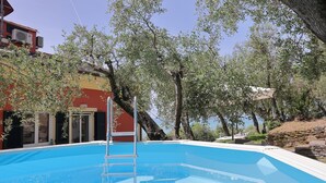 A swimming pool with a ladder, surrounded by trees and a building with a red facade. - Maiso house nestled between the sea and olive trees (Lavagna)