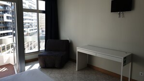 A hotel room with a bed, a desk, a chair, a TV, and a window with a view of buildings. - Tarik  by Atlantichotels (Portimão)