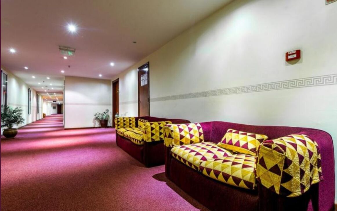 Eine Hotelhalle mit rotem Teppich, einer Couch mit gemusterten Kissen und einem Korridor zu weiteren Zimmern.