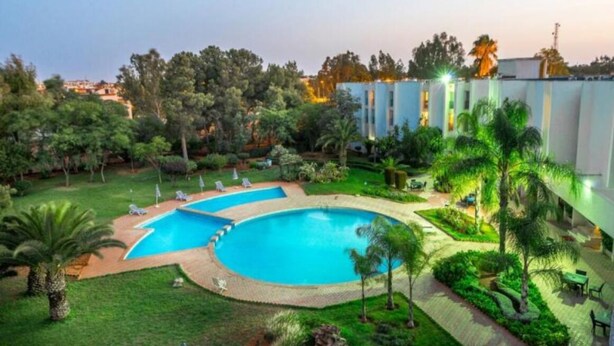 Un resort con un amplio área de piscina, exuberante vegetación y un edificio moderno de varios pisos.