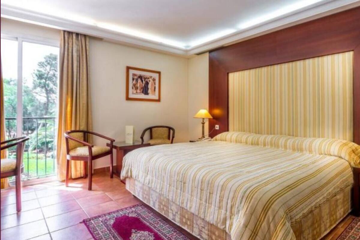 Une chambre d’hôtel avec un grand lit, deux lampes de chevet, une chaise, une petite table et une vue sur l’extérieur.